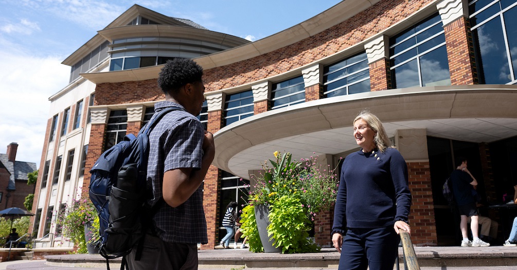 Emily Youatt standing in front of the School of Public Health's building-talking to a student