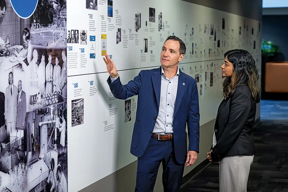 At the NSF world headquarters in Ann Arbor, Pedro Sancha, left, and Swati Sriram view a timeline that highlights the year scientists came together to establish NSF within the University of Michigan School of Public Health.