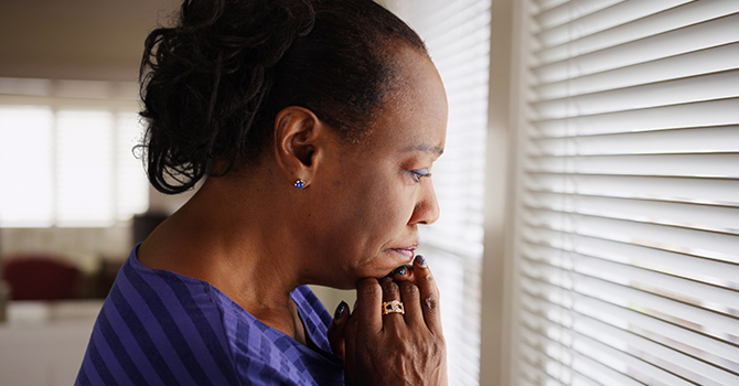 stressed older woman staring through blinds 