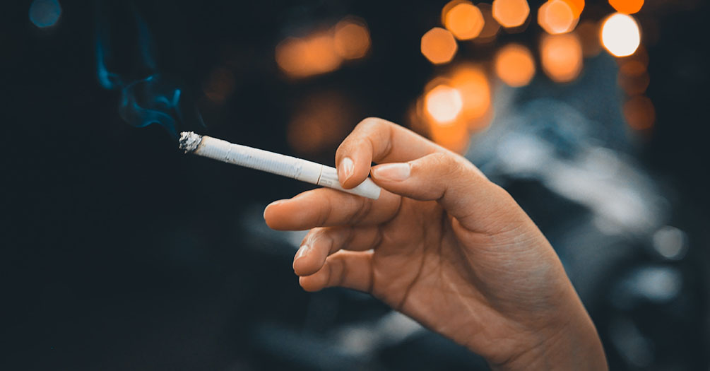 A woman's hand holding a lit cigarette.