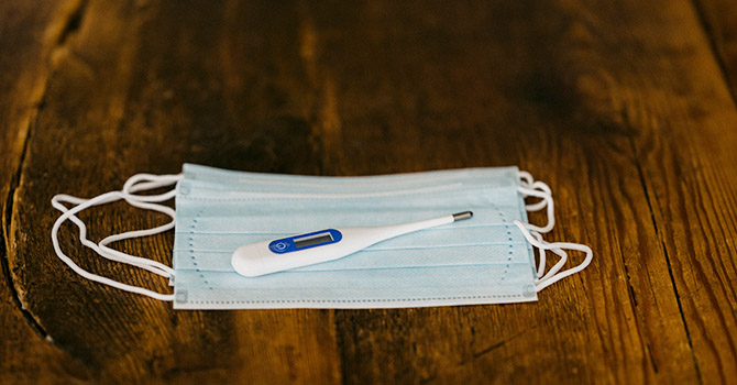 A mask and thermometer placed on a wood table.