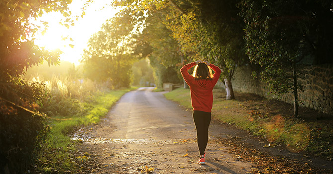 Woman walking on a trail with her hands over her head.