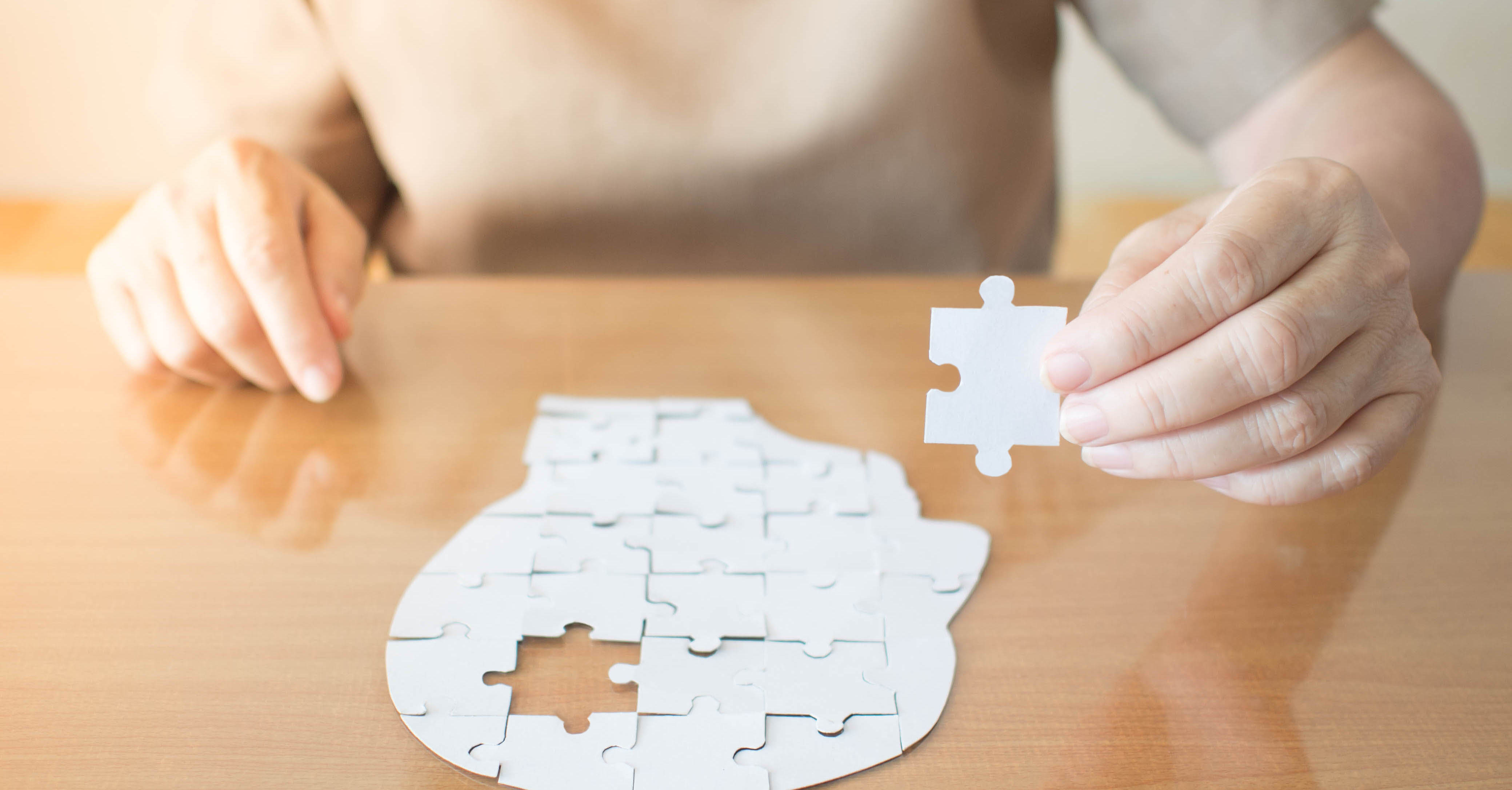 An older adult holding the last puzzle piece to a head-shaped puzzle.