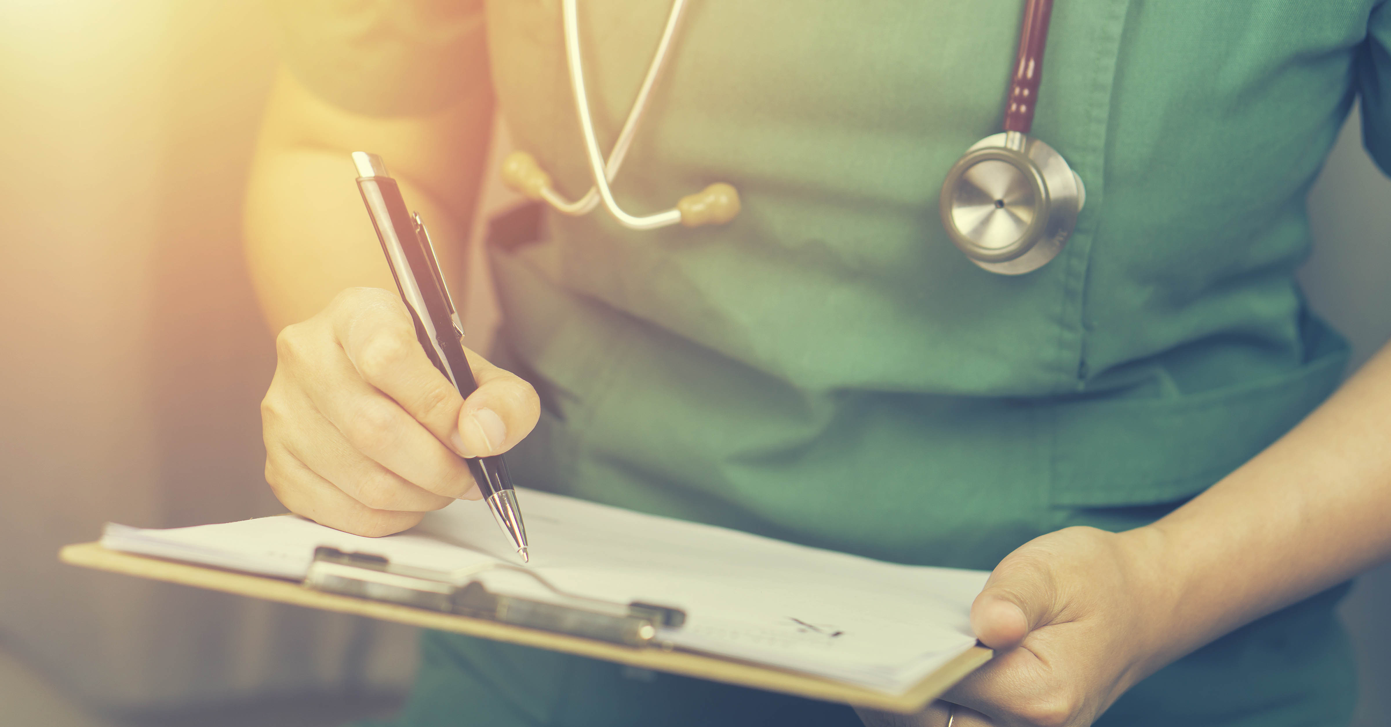 A health care professional fills out a form on a clipboard.