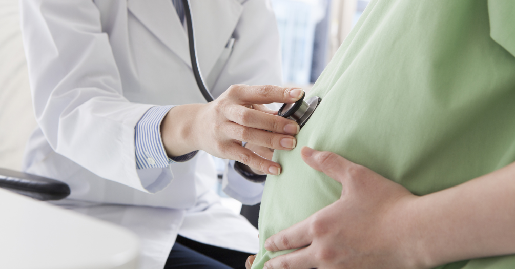 Doctor uses stethoscope to listen to a heartbeat on a pregnant person's stomach