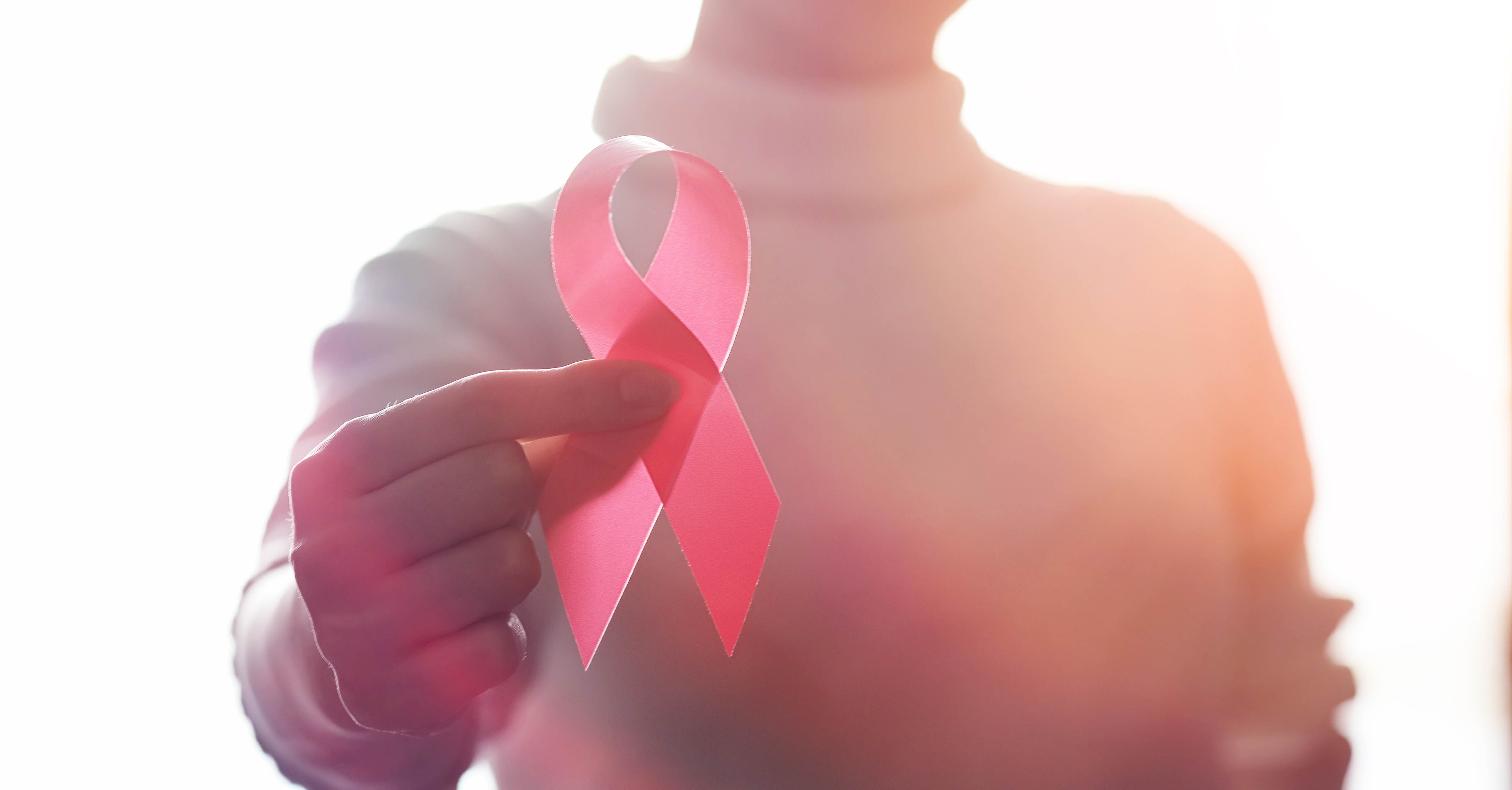 A person holds a red HIV awareness ribbon in their right hand.