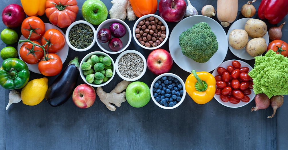 Assorted fresh fruits, vegetables, nuts, and seeds arranged on a dark surface