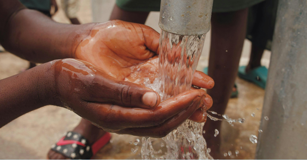 Person washing hands in water pump.