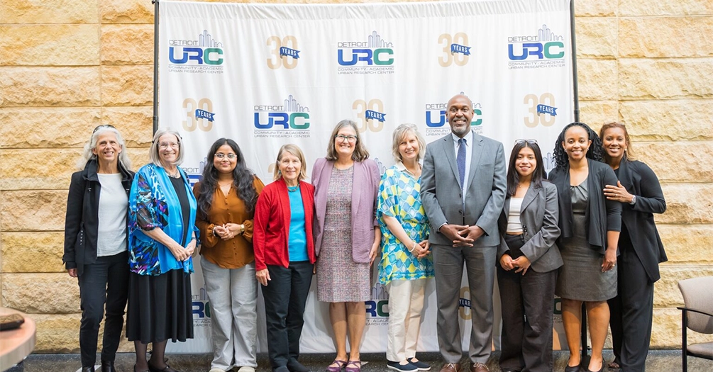 Detroit Urban Research Center faculty, staff, and partners pose together in front of a 30th-anniversary backdrop, marking three decades of community-academic partnership in Detroit.