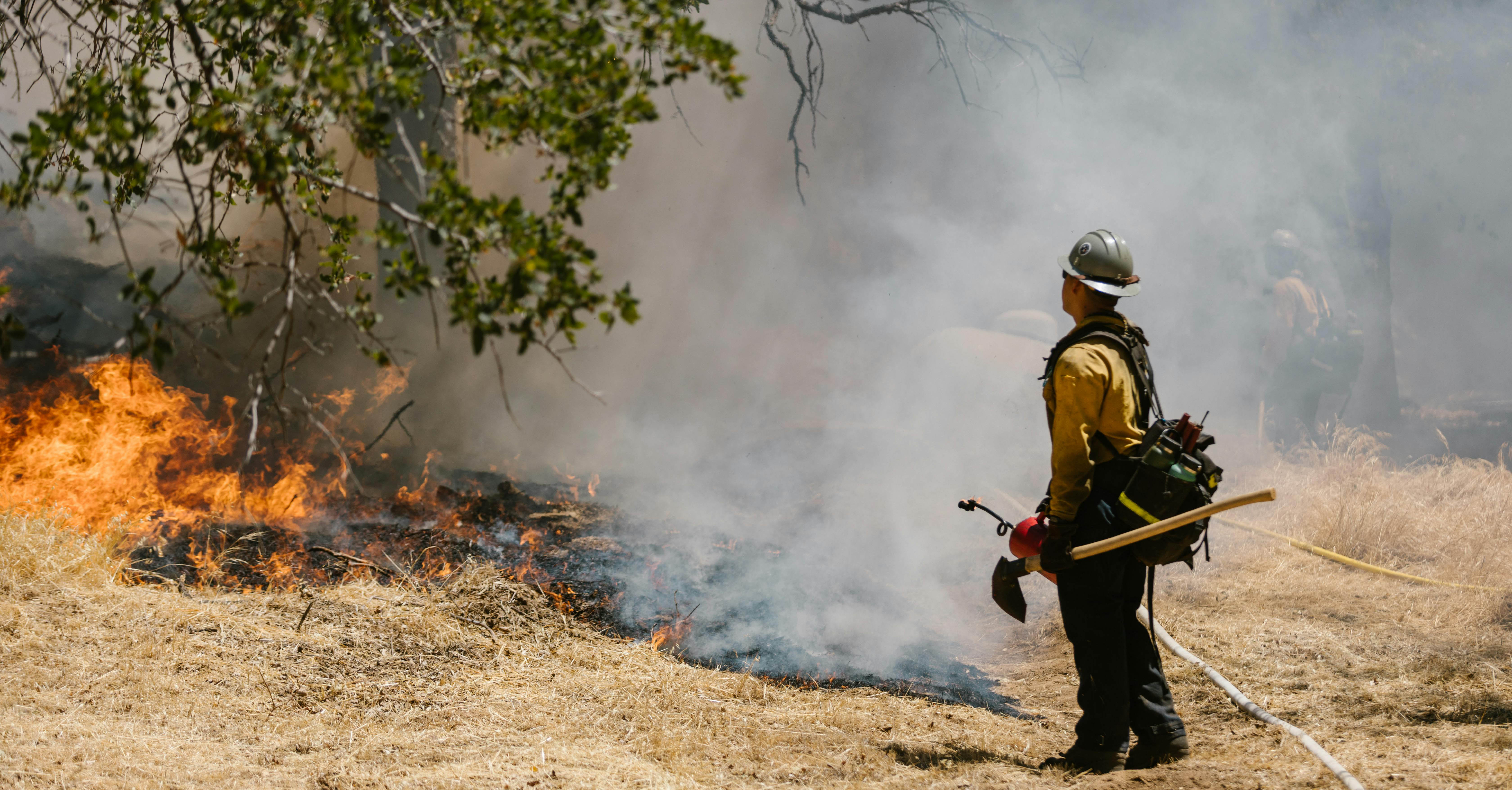 A firefighter stands before a burning wildfire.