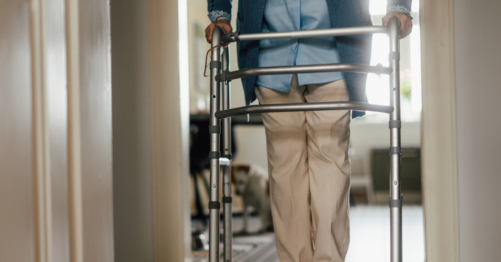 An elderly woman uses a walker for mobility support in her home.