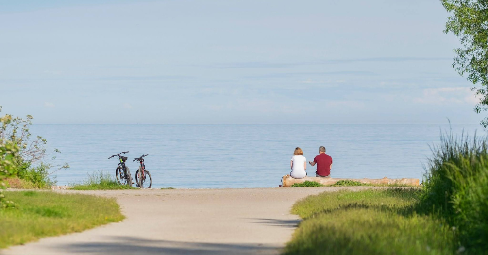 Two older people sit by a lake.