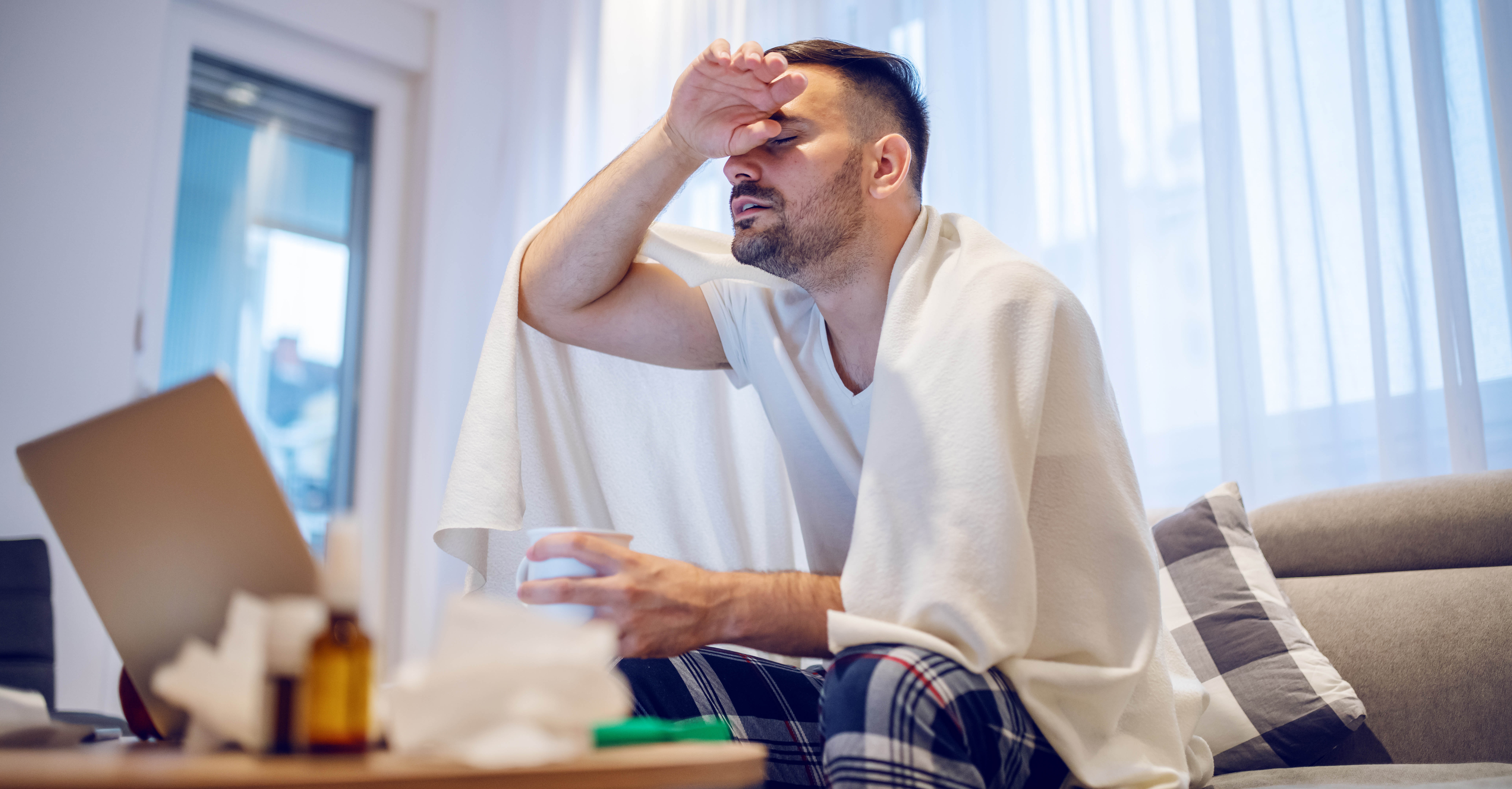 Man holding mug with tea and sitting on sofa in living room.