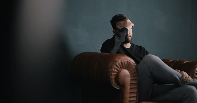 A man holds his head in his left hand while sitting on a leather chair.