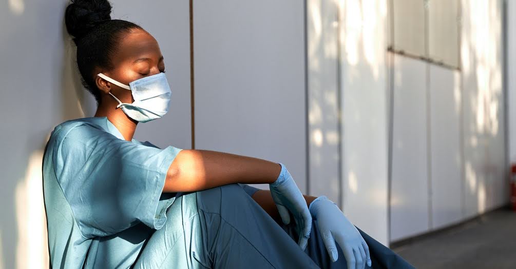 female healthcare worker,  sitting in hospital hallway with a mask on 