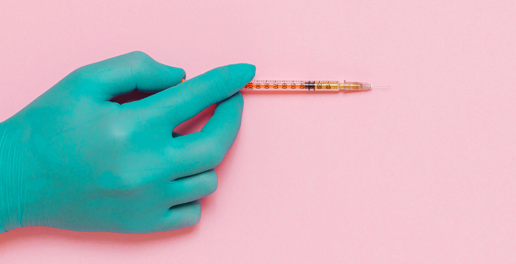 A gloved hand holds a syringe over a pink background