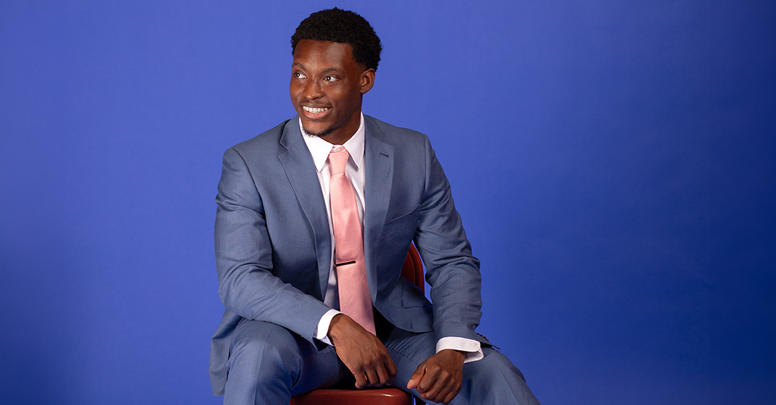 Darius Moore in a blue/gray suit, white shirt sand salmon tie posing for a portrait photo